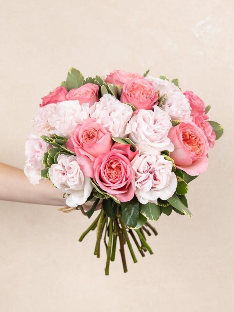 Lush hand-tied bouquet of 23 pink and blush garden roses with layered petals and fresh seasonal greenery, held in a full, rounded arrangement.