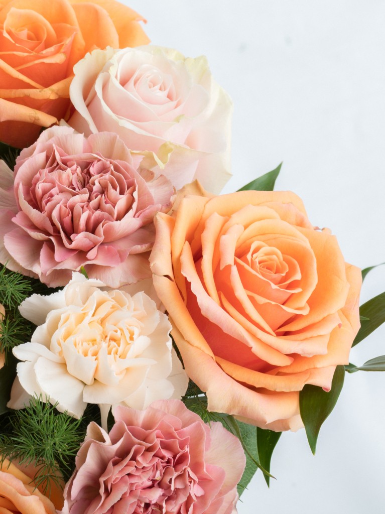 A close-up shot of intricate petal textures and subtle color variations among the apricot roses, blush carnations, and pale pink roses, highlighting the softness and natural detail of each bloom.