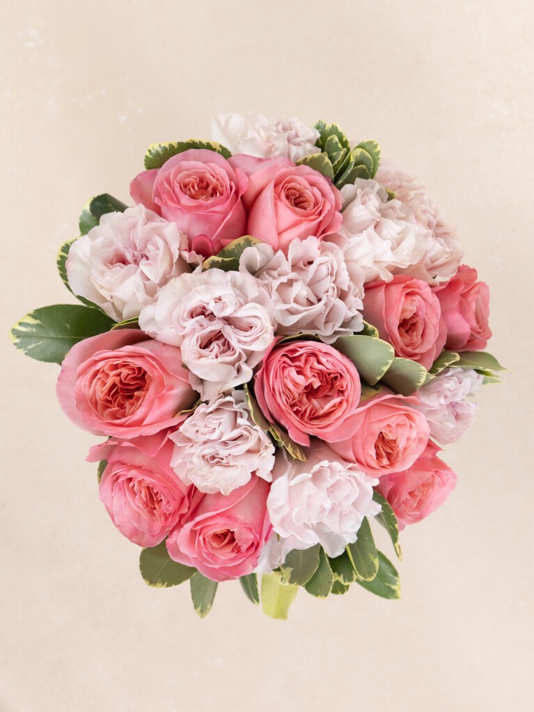 Top view of a rounded 23-stem bouquet with soft pink and blush garden roses, tightly arranged with seasonal greenery in a full, symmetrical composition.